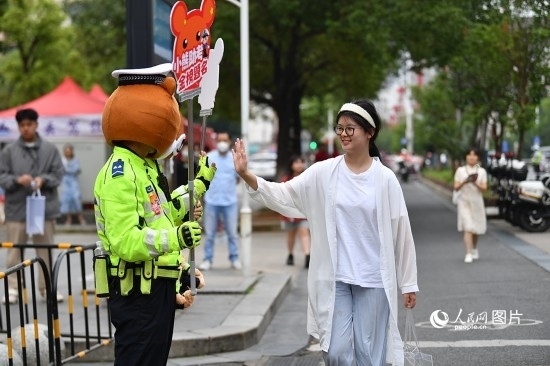 6月7日上午9時，隨著鈴聲的響起，2023年江西高考正式開考，江西省的53.57萬考生以縣（區(qū)）為單位隨機安排在全省256個考點、18968個考場參加高考。圖為“小熊交警”和考生擊掌鼓勵。 人民網記者 時雨攝