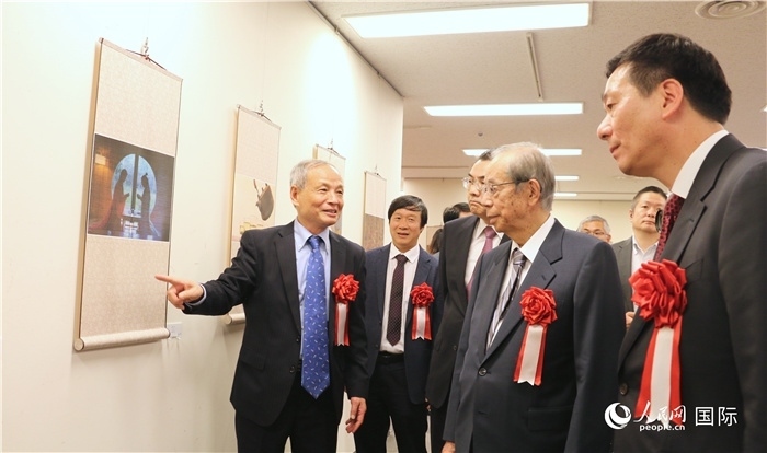 “湖州印象”攝影展主創(chuàng)、世界華人攝影協(xié)會副會長馮學(xué)敏向吳江浩大使、福田康夫前首相等嘉賓介紹展出作品。（人民網(wǎng) 許可攝）