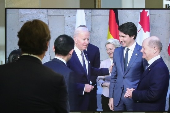 2022年3月24日，在比利時(shí)布魯塞爾的北約總部，一名男子觀看屏幕上美國(guó)總統(tǒng)拜登（右四）、歐盟委員會(huì)主席馮德萊恩（右三）、加拿大總理特魯多（右二）、德國(guó)總理朔爾茨（右一）出席七國(guó)集團(tuán)峰會(huì)合影儀式的畫面。新華社記者鄭煥松攝