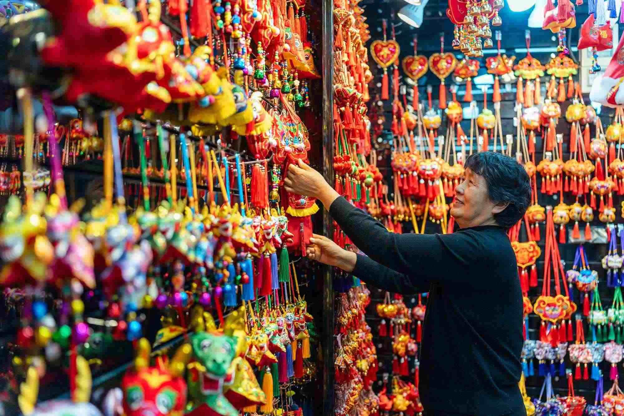 2023年12月11日，金華義烏國際商貿(mào)城，龍年喜慶用品掛滿攤位，顧客正在挑選中。