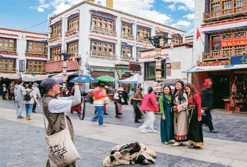 千年八廓街，見(jiàn)證民族團(tuán)結(jié)。2021年7月，習(xí)近平總書(shū)記來(lái)到位于西藏拉薩老城區(qū)的八廓街，感慨地說(shuō)：“千年八廓街，是我們各民族建起來(lái)的八廓街。各民族文化在這里交流交往交融，我們中華民族的大家庭在這里其樂(lè)融融。”圖為2023年6月13日，游客身著藏裝在八廓街拍照留念。 新華社記者 姜帆/攝