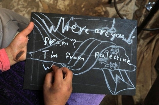 2023年12月28日，一名學生在加沙地帶南部城市拉法一所學校的臨時教室中寫下“我來自巴勒斯坦”的字樣。新華社發(fā)（里澤克·阿卜杜勒賈瓦德攝）