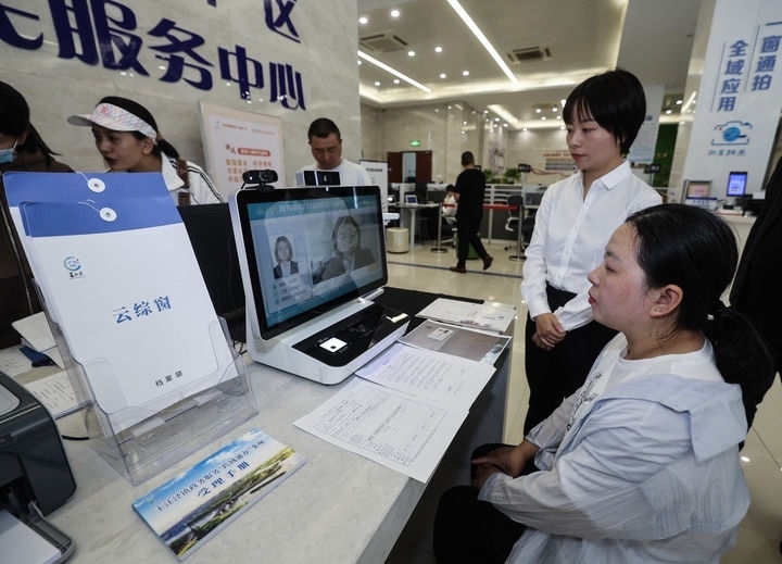 在浙江省嘉興市秀洲區(qū)王江涇鎮(zhèn)便民服務中心的“跨域通辦·云綜窗”窗口，辦理開業(yè)登記的個體工商戶（右一）通過該系統(tǒng)與江蘇省蘇州市吳江區(qū)盛澤鎮(zhèn)行政審批局工作人員視頻連線，進行身份讀取及材料線上審核（2024年5月9日攝）。新華社記者 徐昱 攝