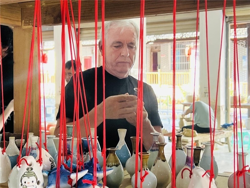 鄉(xiāng)愁如同一根根紅線，將游子與故鄉(xiāng)永遠(yuǎn)地牽連到一起。花茂村陶藝文化創(chuàng)意一條街的母氏陶藝館內(nèi)，紅線吊著陶瓶，思緒游走萬(wàn)里。摩爾多瓦“信息標(biāo)簽”通訊社社長(zhǎng)亞歷山大·塔納斯端詳著館內(nèi)展示的陶藝作品，并挑選出心儀的小擺件帶回摩爾多瓦，也帶走花茂村的“鄉(xiāng)愁”。（張亞欣攝）