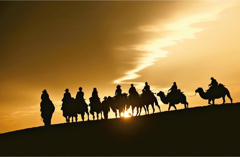 新時(shí)代以來(lái)，文化和旅游深度融合發(fā)展體制機(jī)制不斷健全，成功走出了一條獨(dú)具特色的中國(guó)旅游發(fā)展之路。圖為2024年9月1日清晨，游客在甘肅省敦煌市鳴沙山月牙泉景區(qū)乘騎駱駝，欣賞大漠風(fēng)光，體驗(yàn)絲路風(fēng)情。 新華社發(fā) 張曉亮/攝