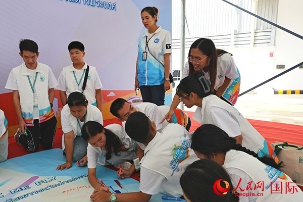 泰國學(xué)生在開營儀式展板上繪制圖案。人民網(wǎng)記者 白元琪攝