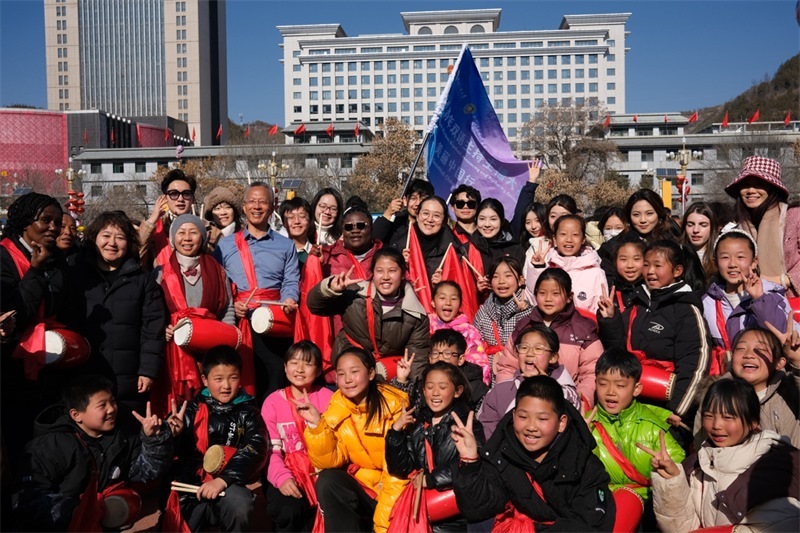 中外青年學(xué)子在安塞文化廣場觀看陜北腰鼓和大秧歌表演后合影留念，大家踏著鼓點共舞，翻飛的紅綢與躍動的身影交織，在黃土地廣場上繪出一幅生動的陜北民俗互動畫卷